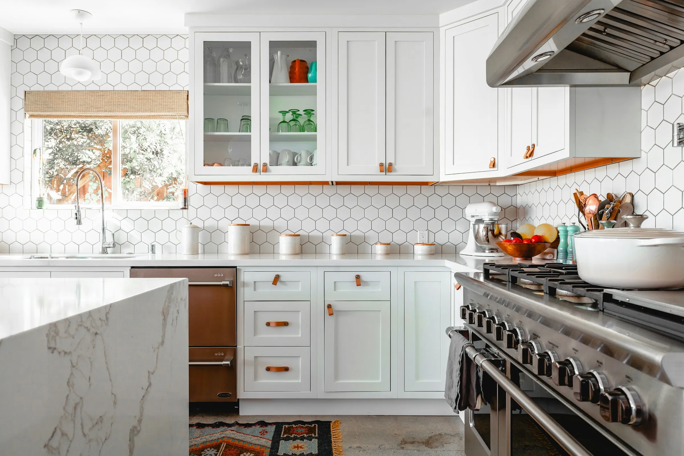 A sunlit kitchen with white cabinetry and a polished marble counter