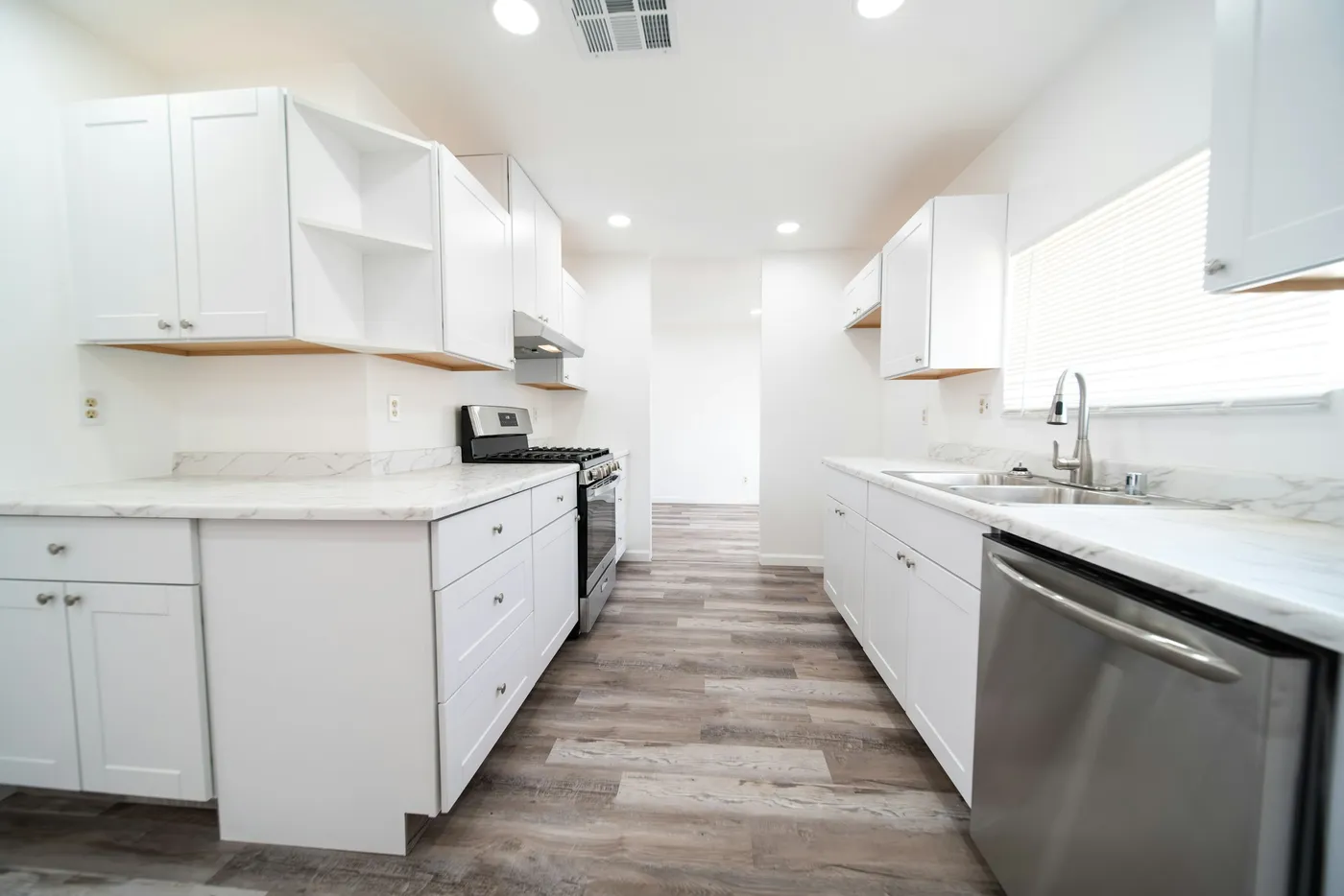 A fully empty kitchen with white cabinets and stainless appliances, ready for new tenants