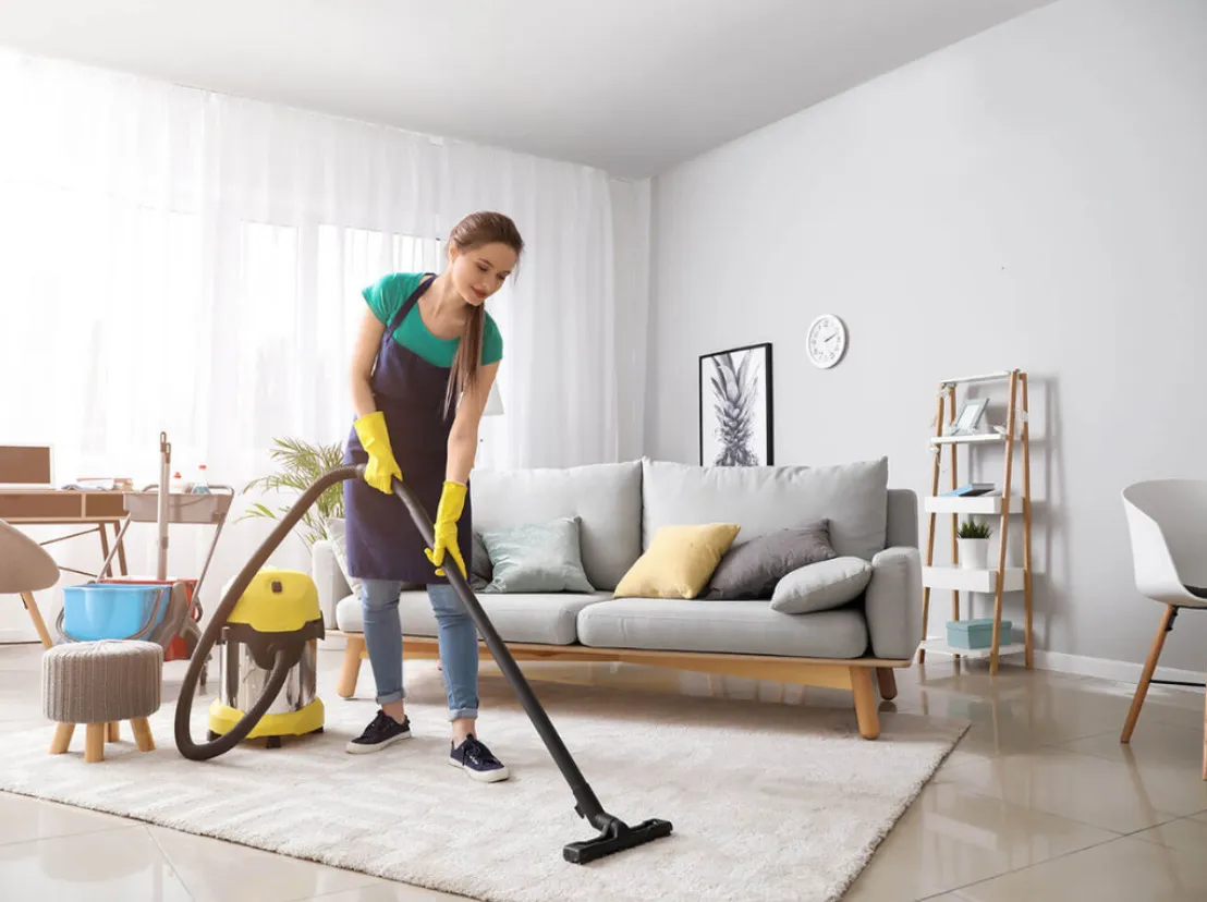 A cleaner vacuuming a rug in a bright, tidy living room